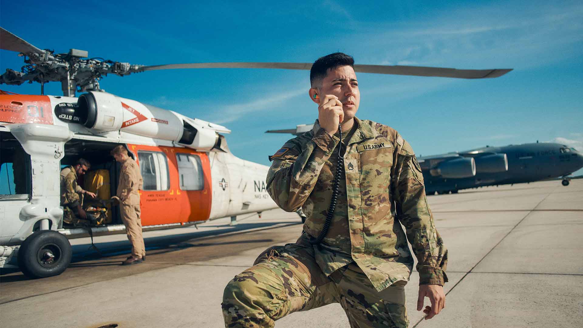Juan Canas, taking a knee and using a radio in front of a helicopter