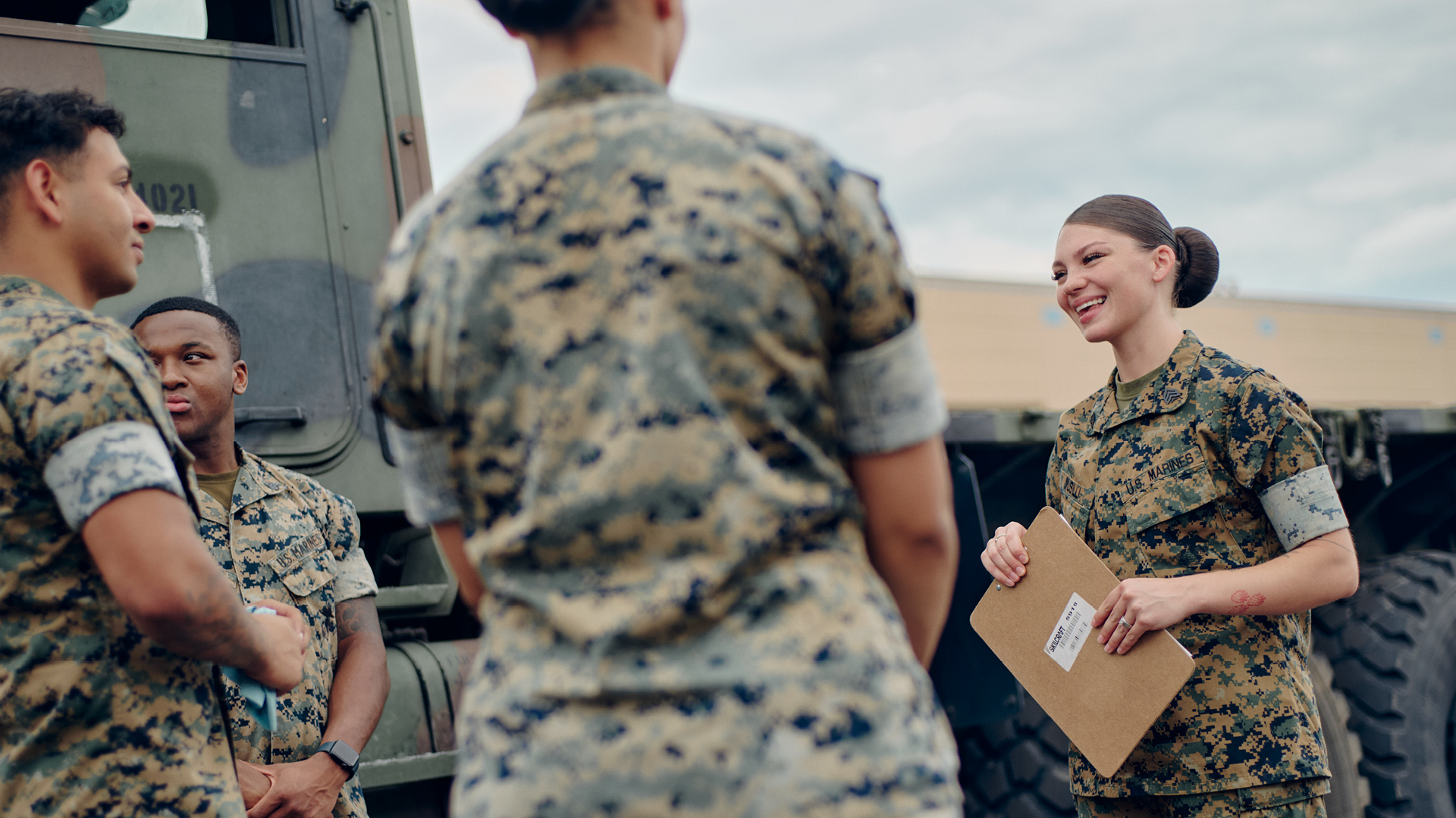 Mackenzie Musilli holding a clipboard and talking with other service members in front of a tactical truck.