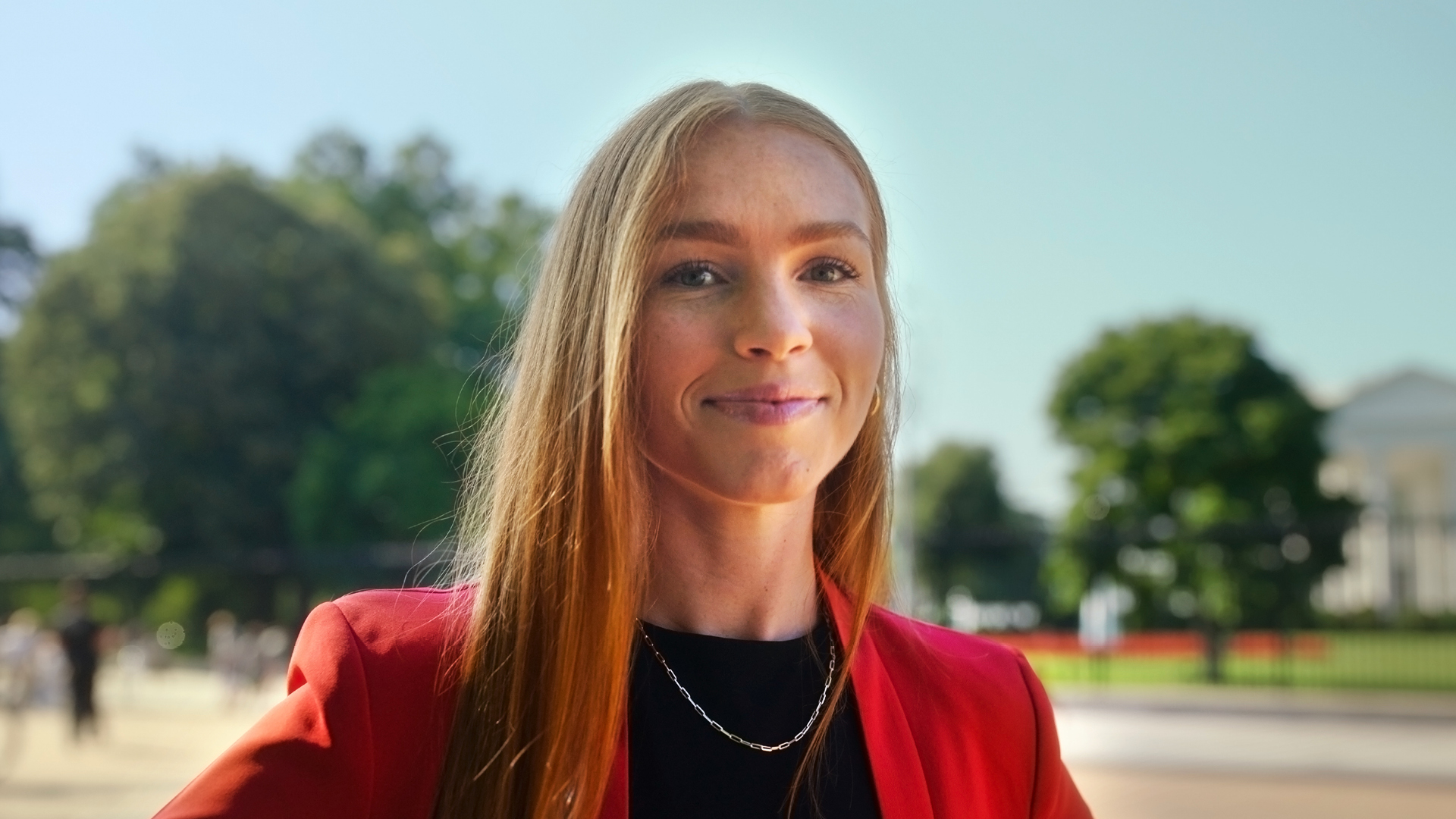 A portrait of Taylor DeHoratiis wearing a red blazer outdoors in Washington, D.C.